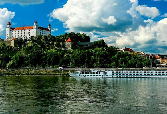 A boat is floating on the water in front of a castle on a hill in Bratislava