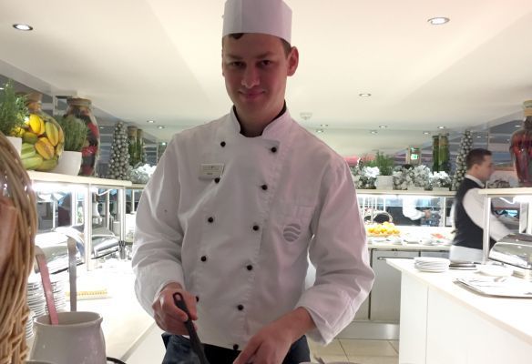 A man in a chef 's uniform is standing in a kitchen