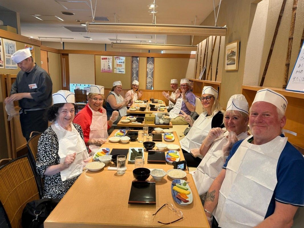 People in a Japanese restaurant wearing hats and aprons at a table. A chef prepares food.