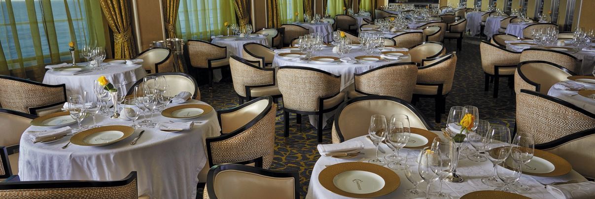 A large dining room filled with tables and chairs set for a formal french dinner on seven seas voyager