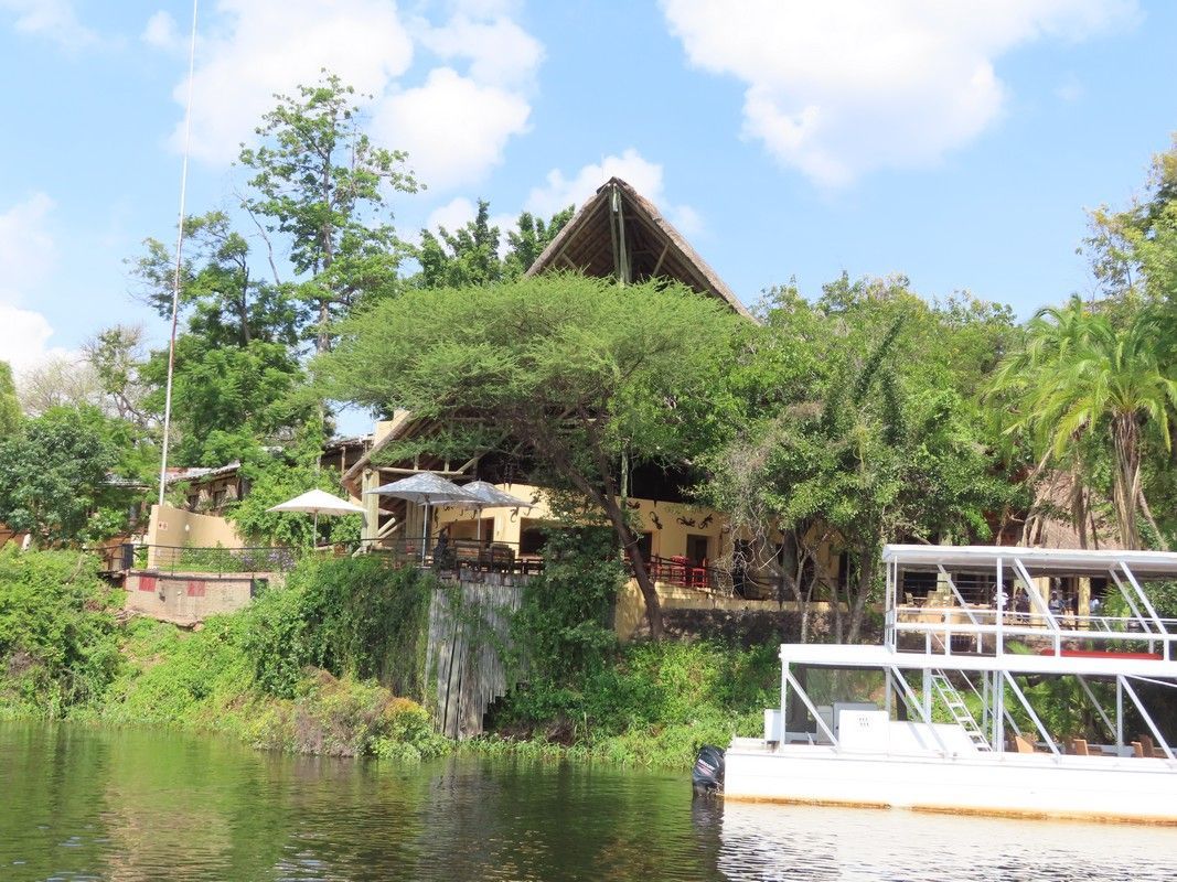 A boat is floating on a river in front of a building surrounded by trees.