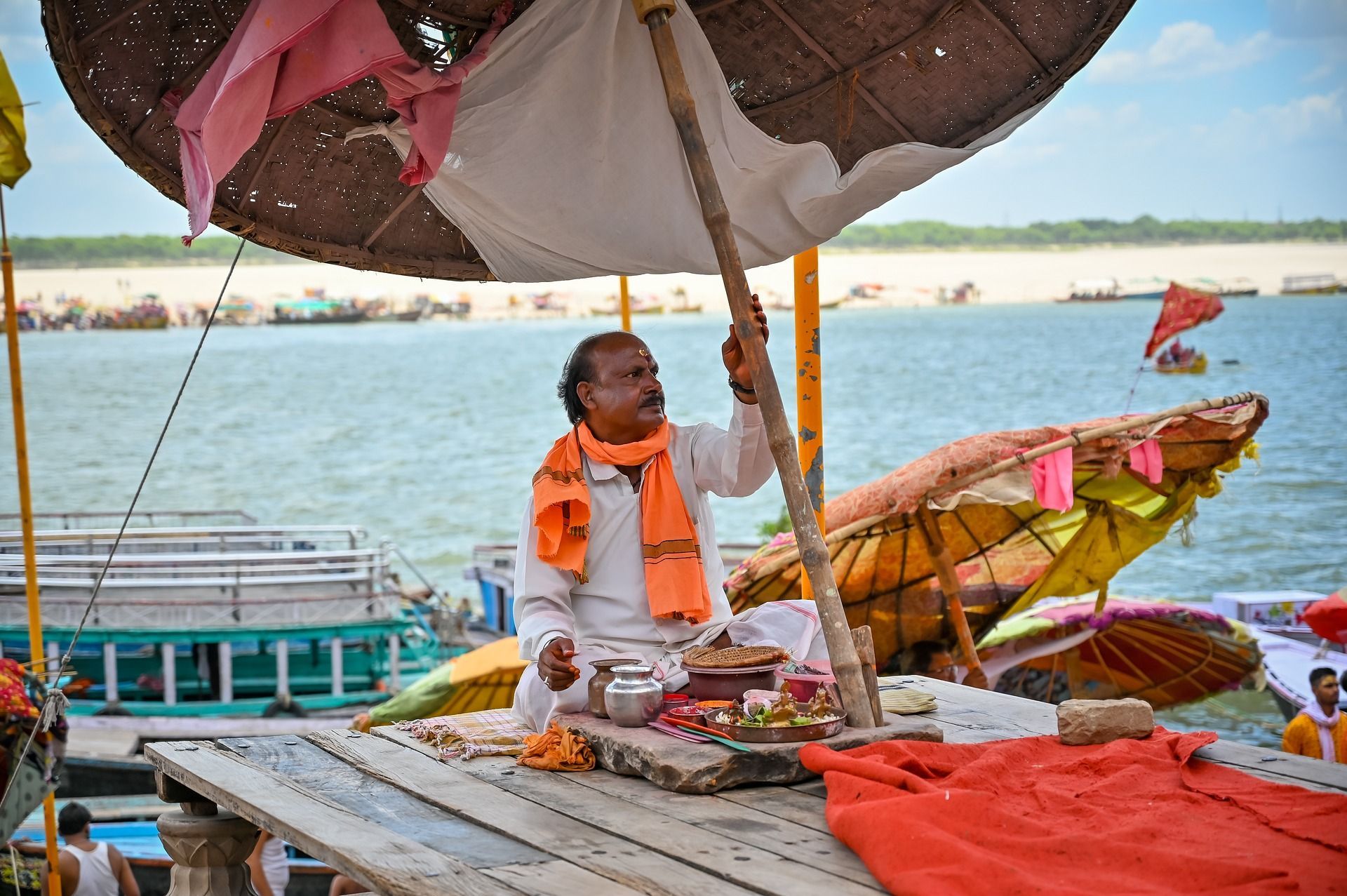 A man is sitting under an umbrella next to Ganges river.