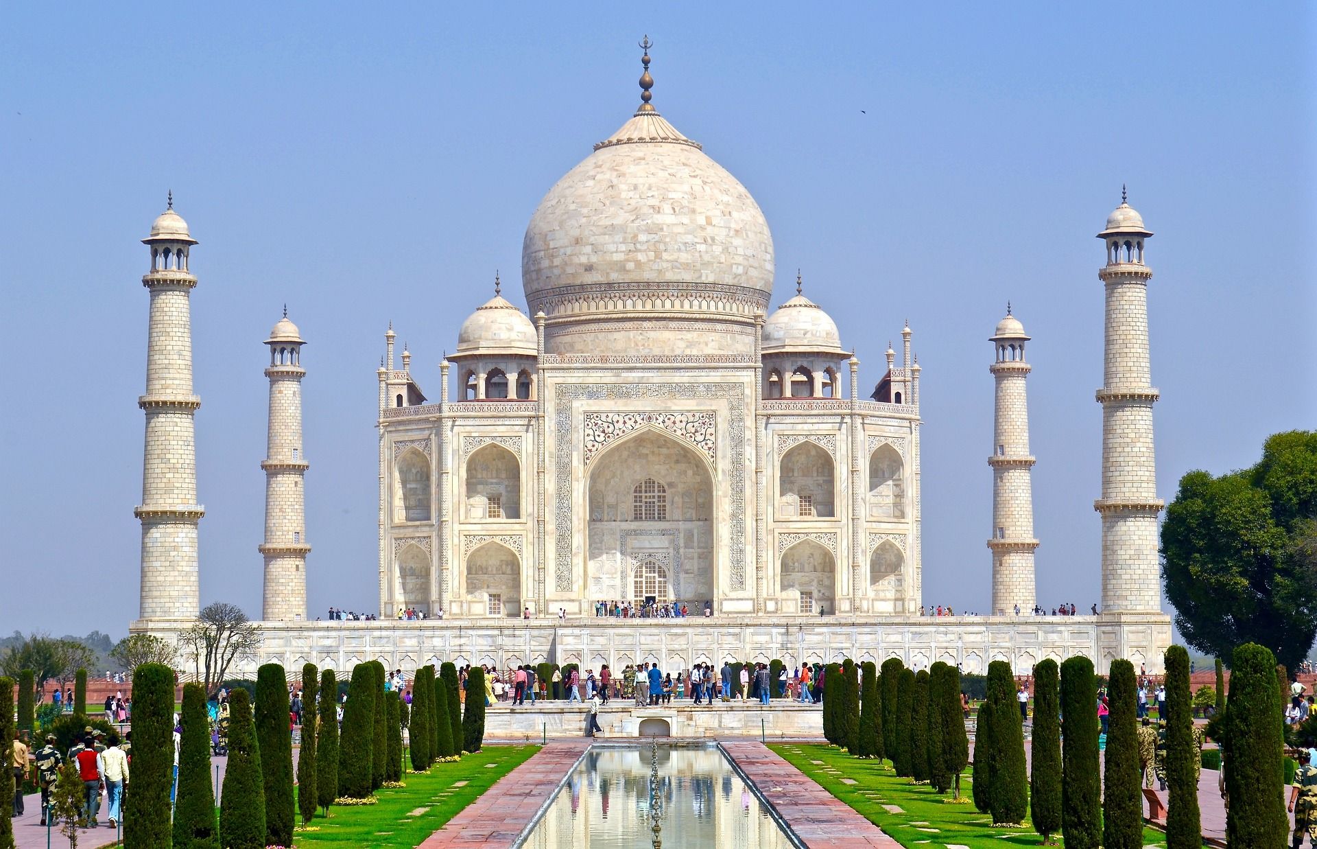 A large white building with a dome is surrounded by trees and a fountain in India