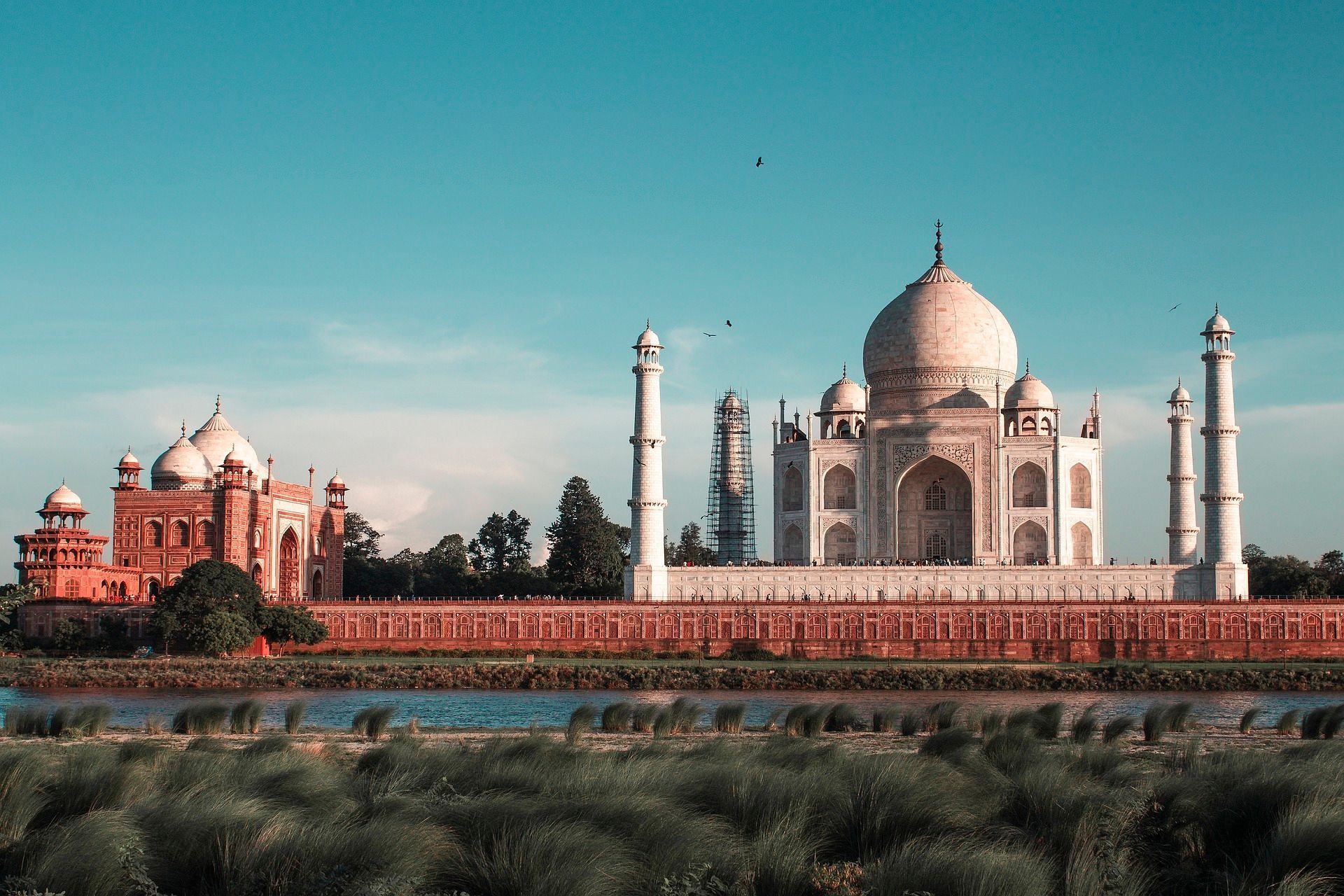 The taj mahal is a very large building sitting next to a body of water.