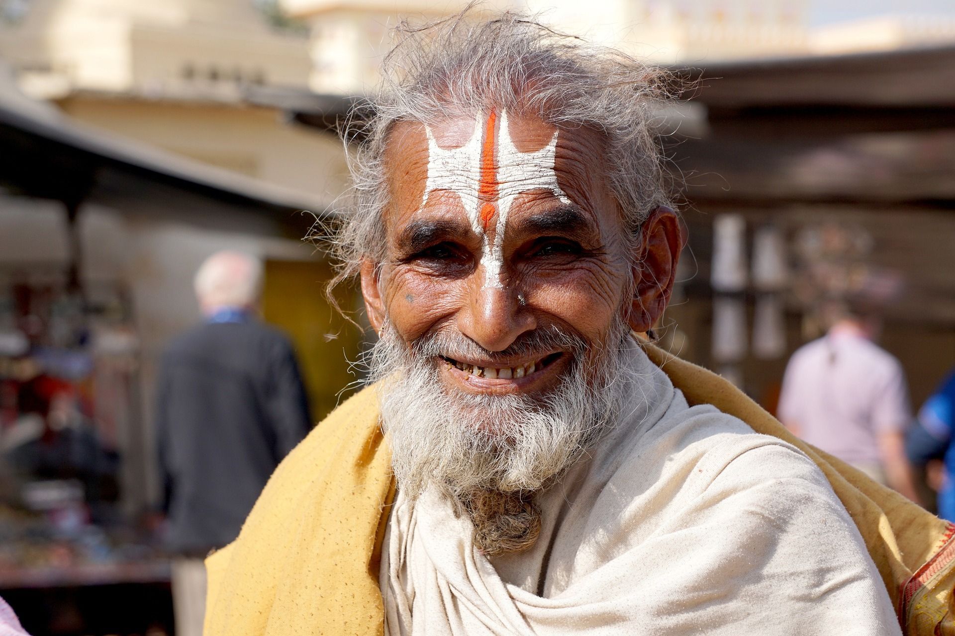 A man with a beard and a crown painted on his forehead is smiling.