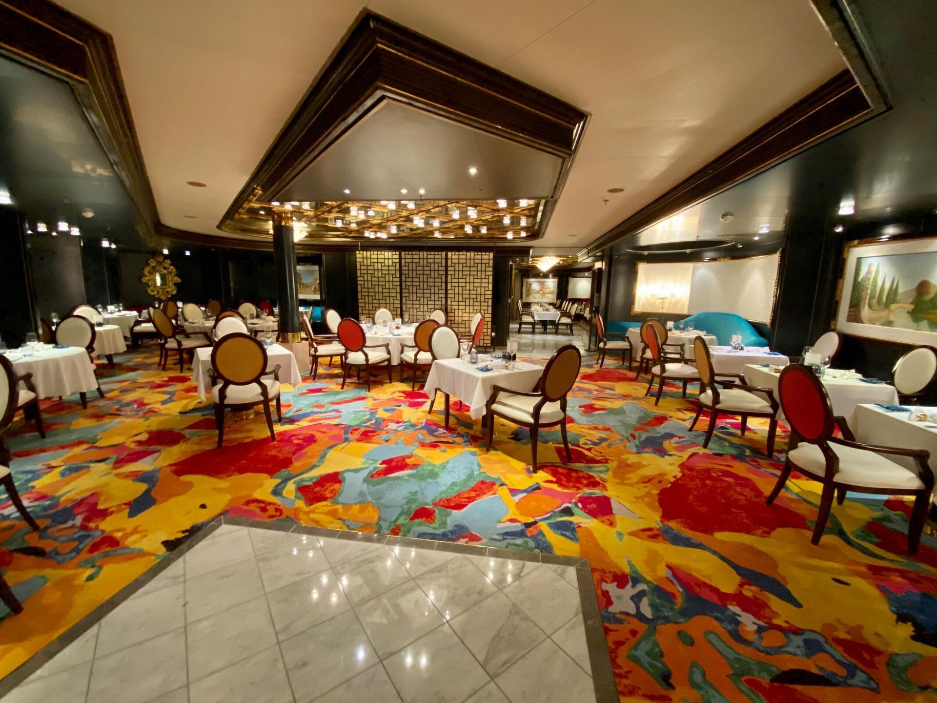 A large dining room with tables and chairs and a colorful rug