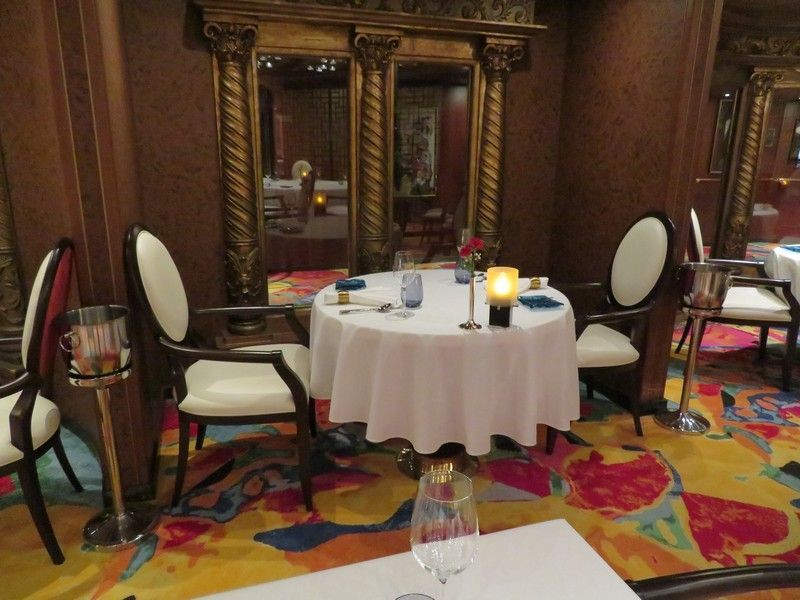 A dining room with a table and chairs and a glass of wine