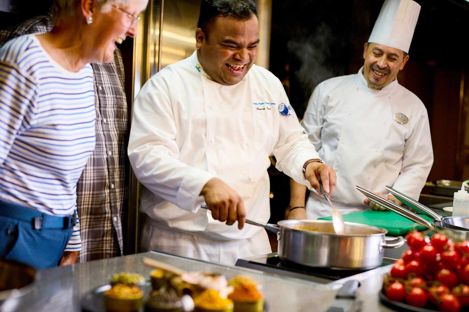 A group of chefs are preparing food in a kitchen while a woman watches.