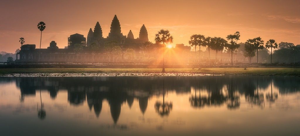 A temple skyline is reflected in a lake at sunset.