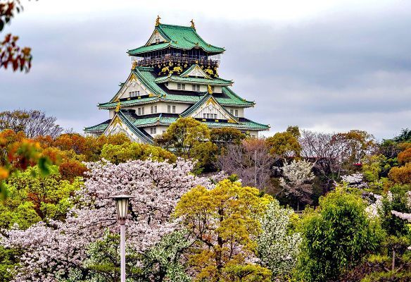 A Japanese castle with a green roof is surrounded by trees and flowers.