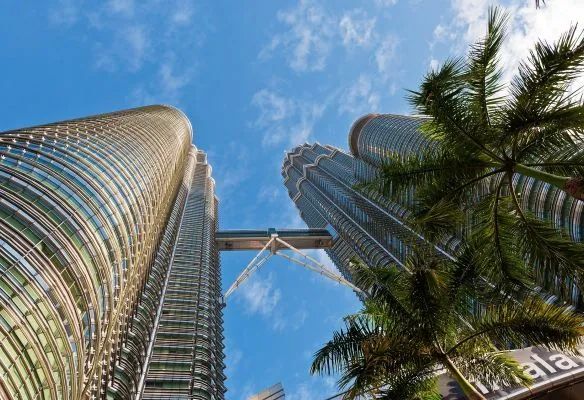 Looking up at two tall buildings with palm trees in front of them in Kuala Lumpur