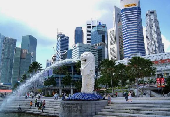 A statue of a lion is spraying water in front of singapore city skyline