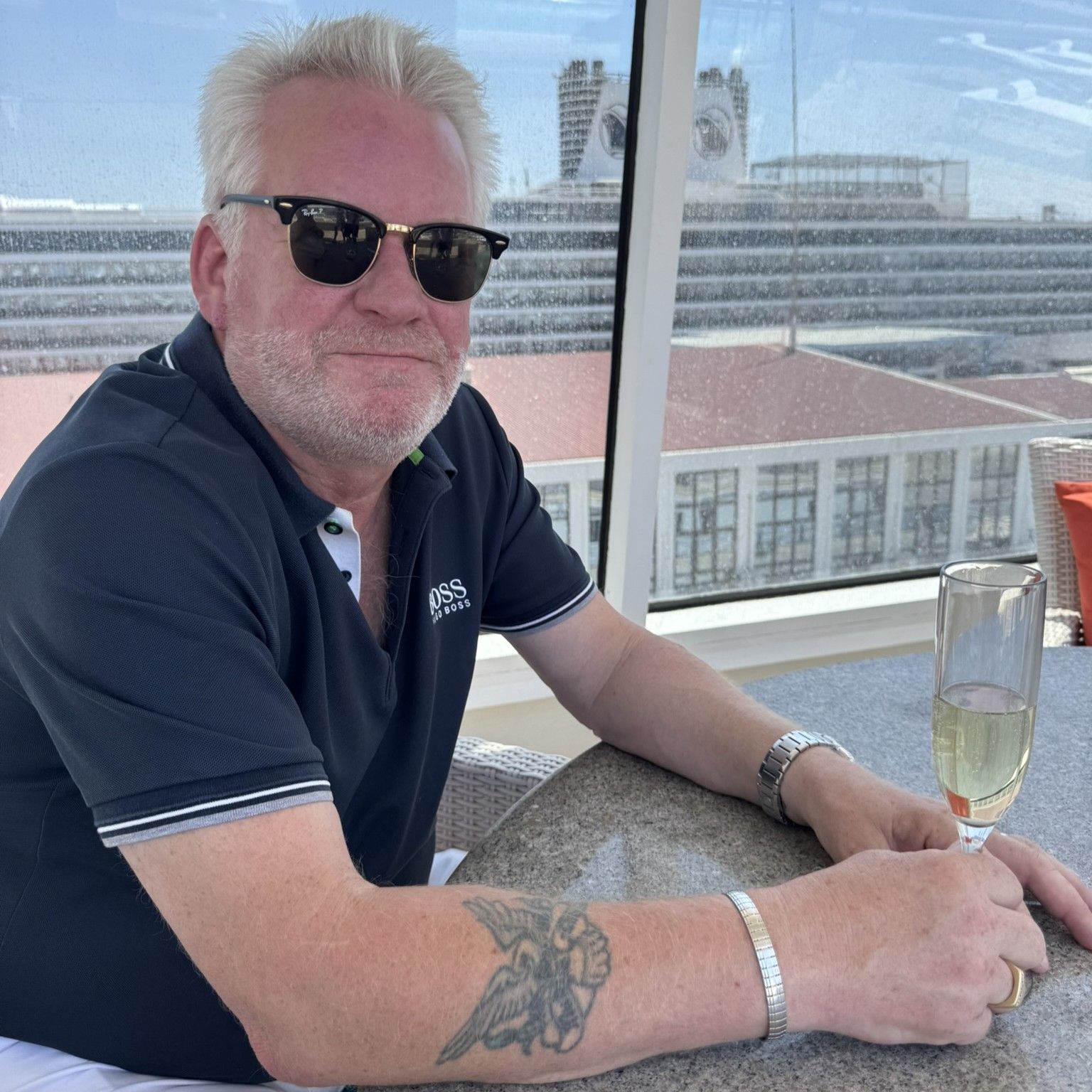 Man in sunglasses, drinks, with a cruise ship background.