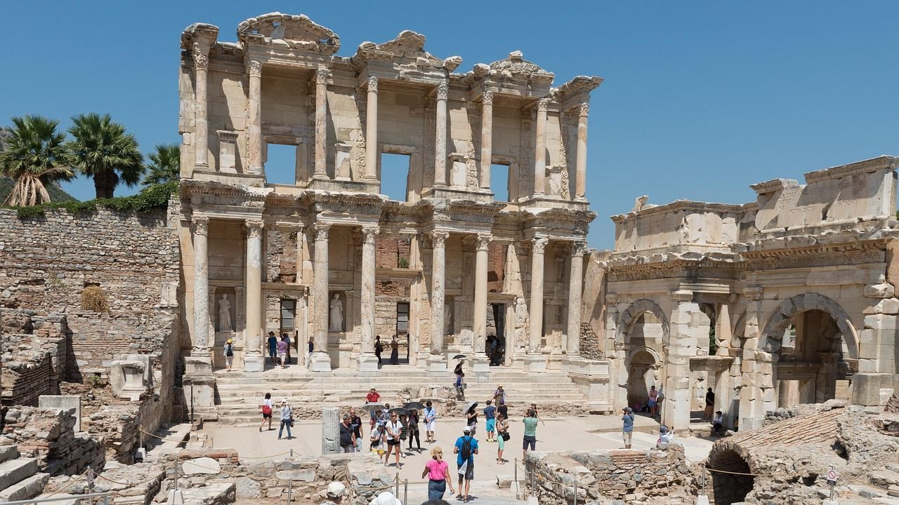 Ruins of the Library of Celsus in Ephesus, Turkey, with tourists and a clear blue sky.