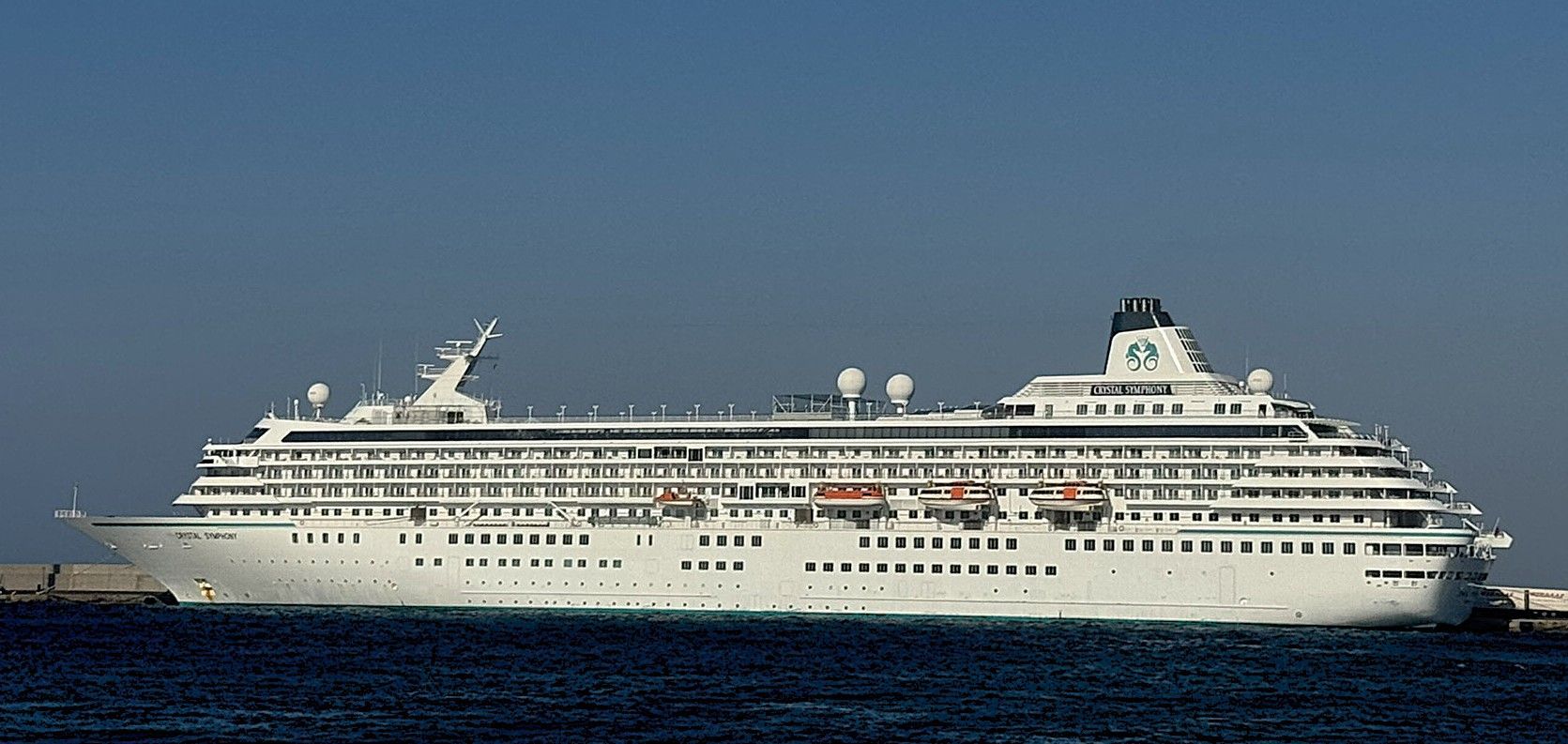A white cruise ship sailing on blue water under a clear blue sky.