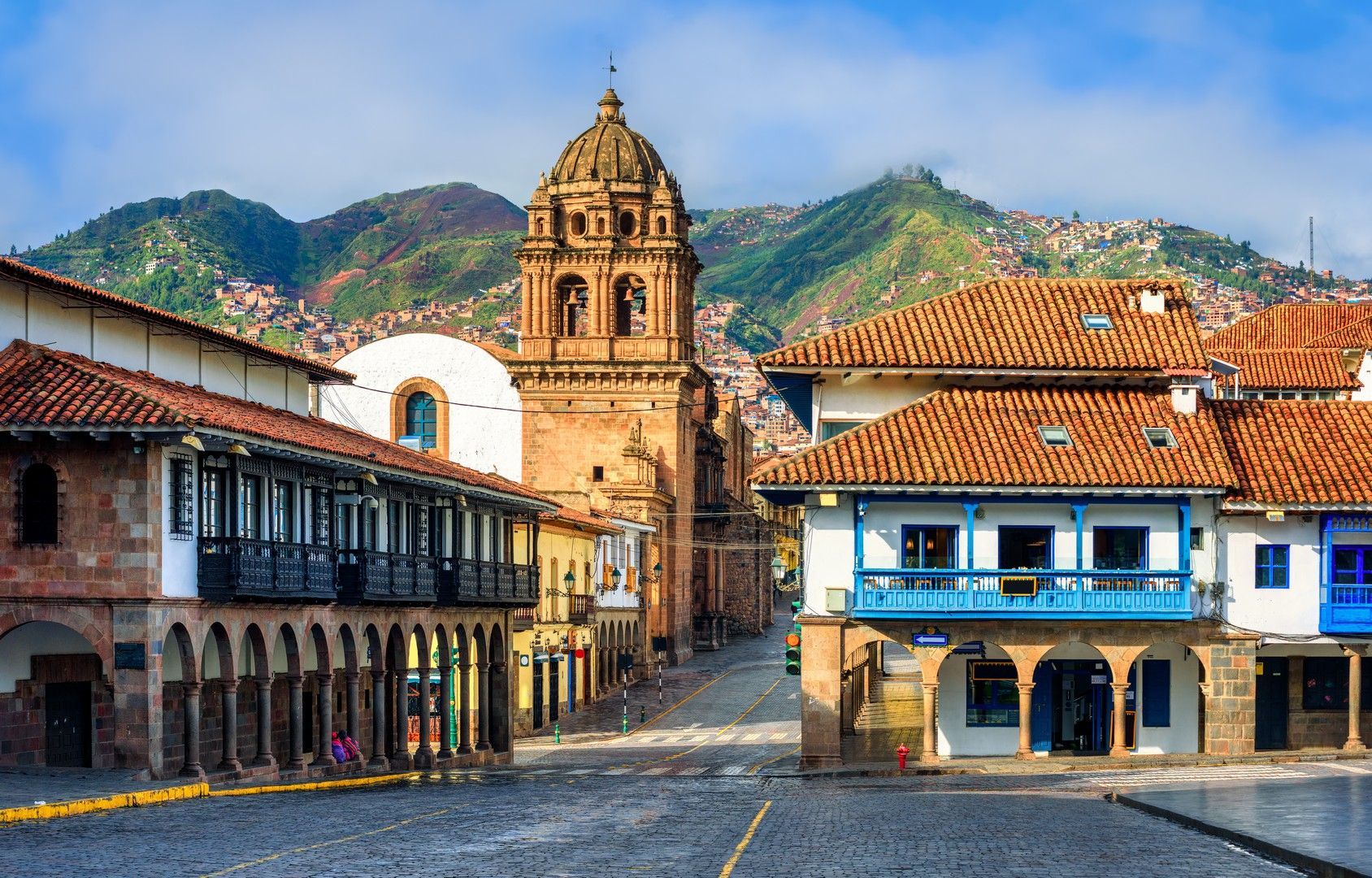 A row of buildings with a church in the background and mountains in the background in Cusco, Peru