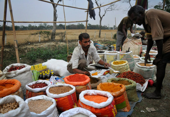 A man is sitting at a table surrounded by bags of spices in India