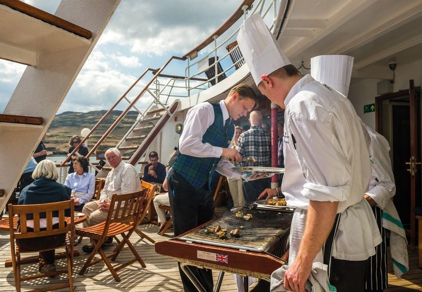 Two chefs are preparing BBQ food on the deck of a cruise ship.