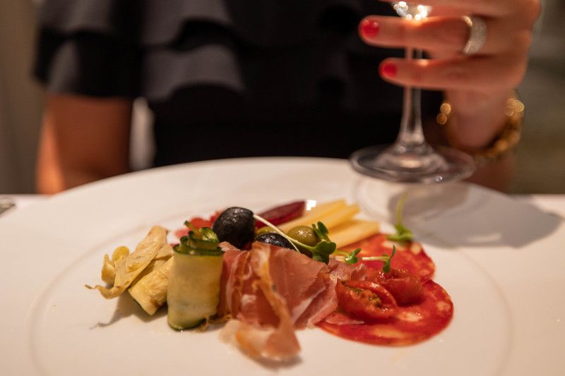 A woman is sitting at a table with a plate of food and a glass of wine in Aqualina.