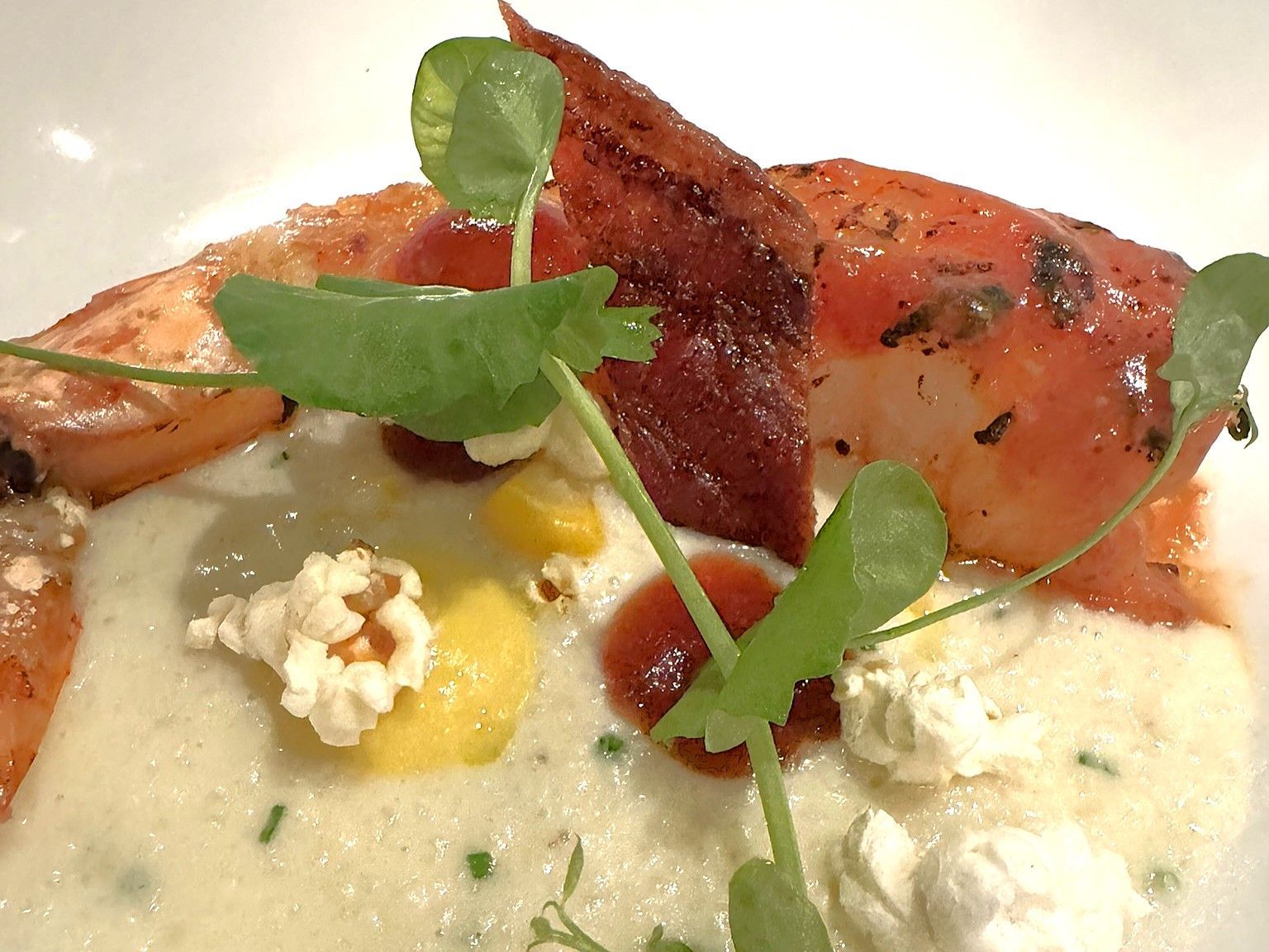 Close-up of gourmet seafood dish with a creamy sauce, bacon, herbs, and popcorn garnish.