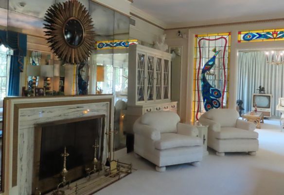 The lounge at Graceland, a living room with a fireplace , chairs and a stained glass peacock window .