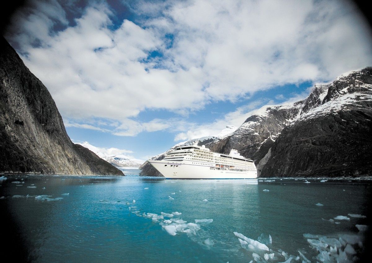 A cruise ship is in the middle of a body of water surrounded by mountains