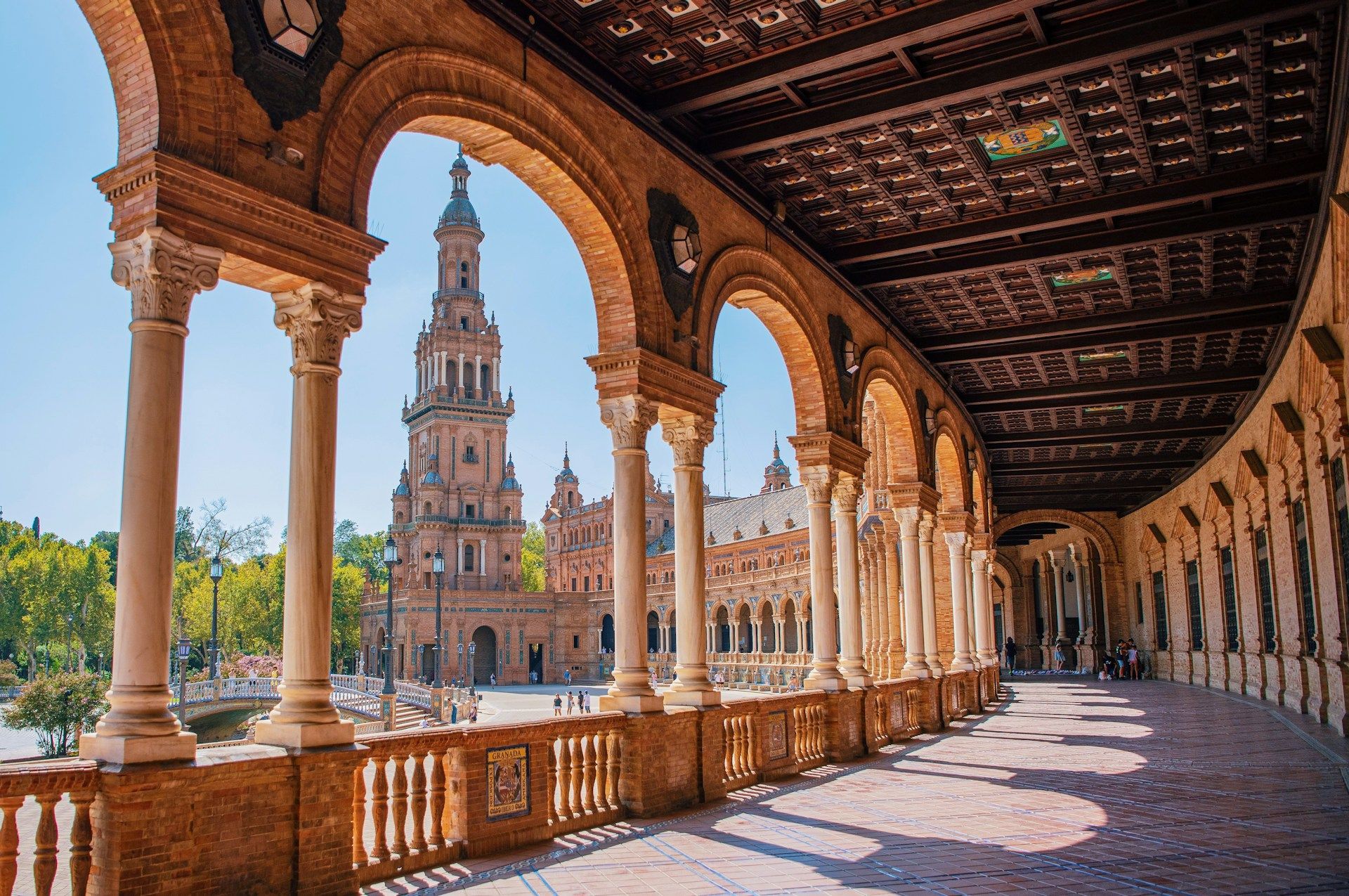 Discover the European Film Festival, Seville only with Azamara Ornate arched walkway with view of a tall brick tower in Seville, Spain, under a blue sky.