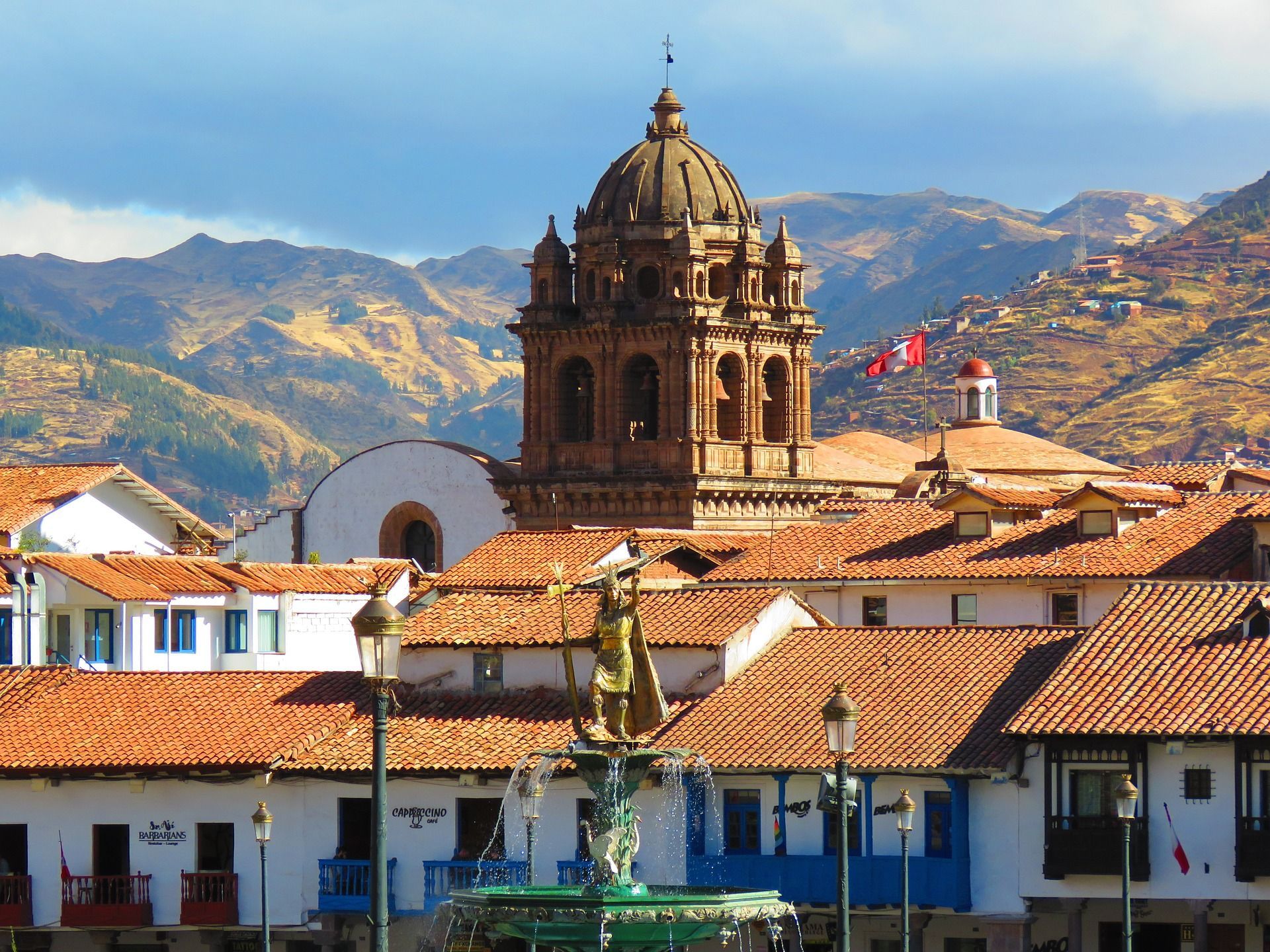 A fountain in front of a church with mountains in the background in Cusco