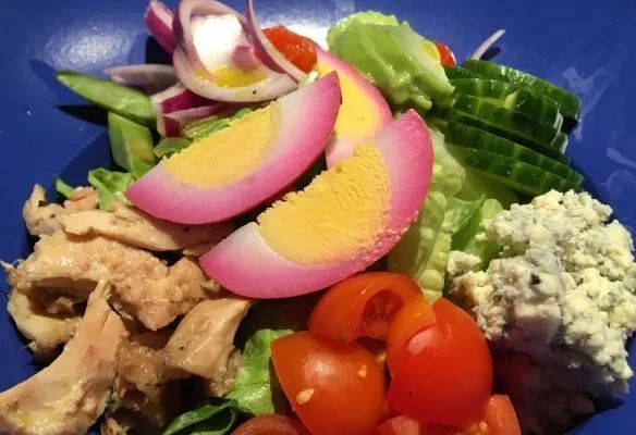 A close up of a salad with tomatoes onions and eggs on a blue plate