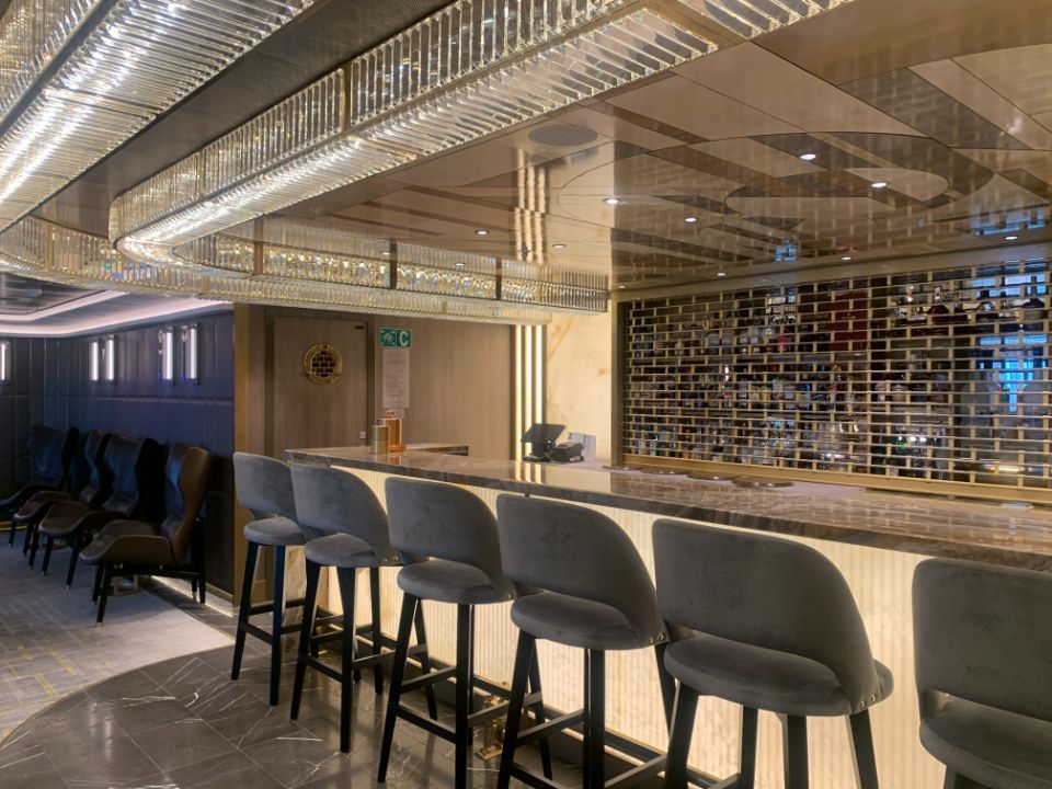 A row of bar stools are lined up in front of a long bar 