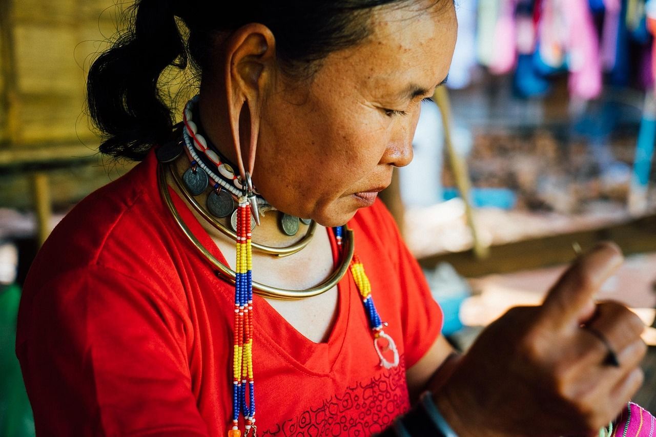 A woman wearing a red shirt and earrings is using a cell phone.