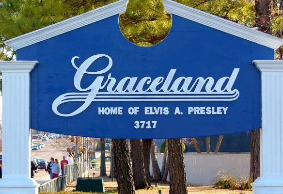 a blue sign that says `` graceland home of elvis a. presley '' is surrounded by trees .