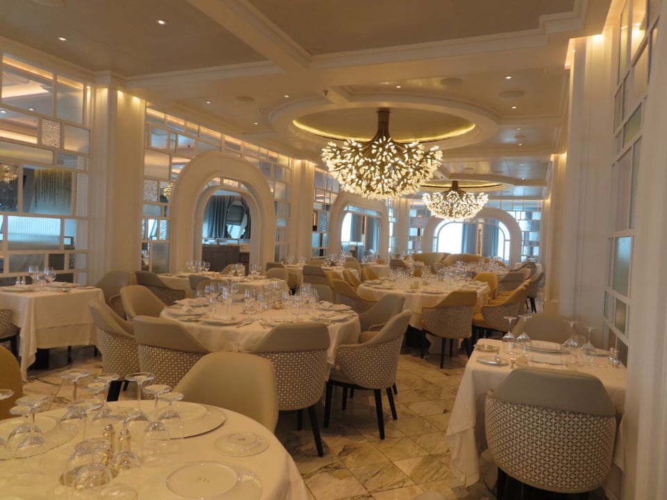 A large dining room with tables and chairs and a chandelier hanging from the ceiling.