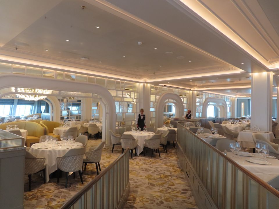 A large dining room with tables and chairs on a cruise ship.