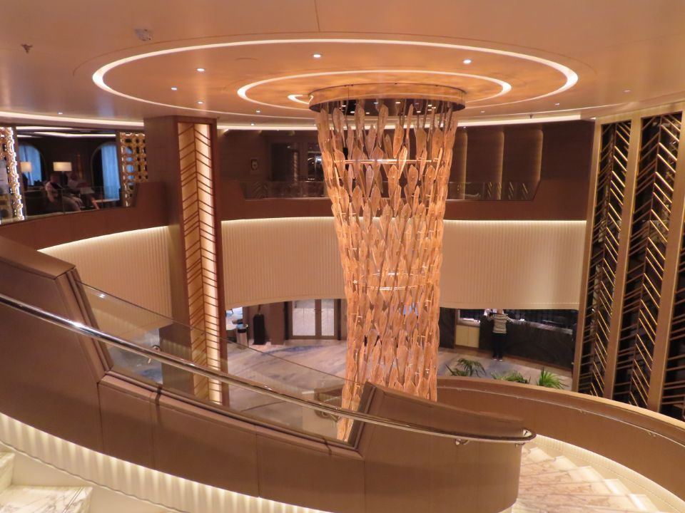 A large chandelier is hanging from the ceiling of a cruise ship lobby.