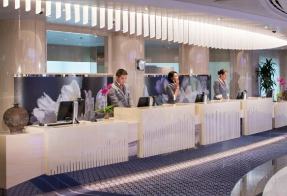 a group of people are standing at a cruise ship reception desk on Holland America Lines Koningsdam.