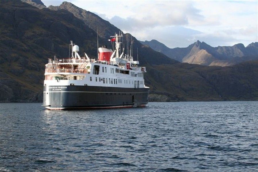 Hebridean Princess at anchor Cruise ship on water in front of a mountainous landscape.