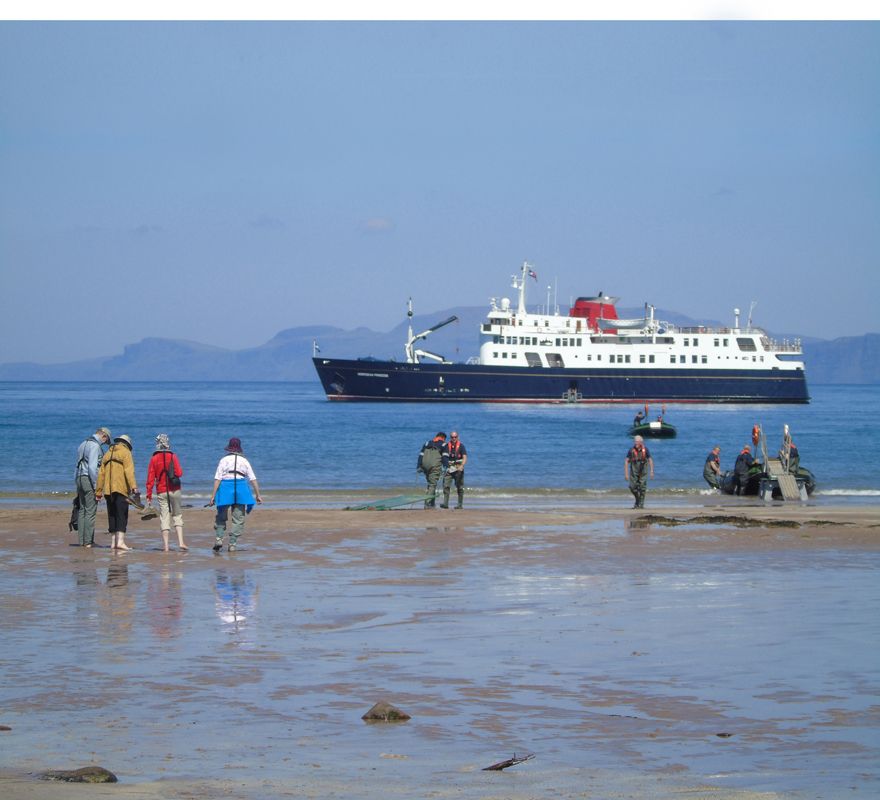 A group of people walking on a beach with a ship called Hebridean Princess in the background