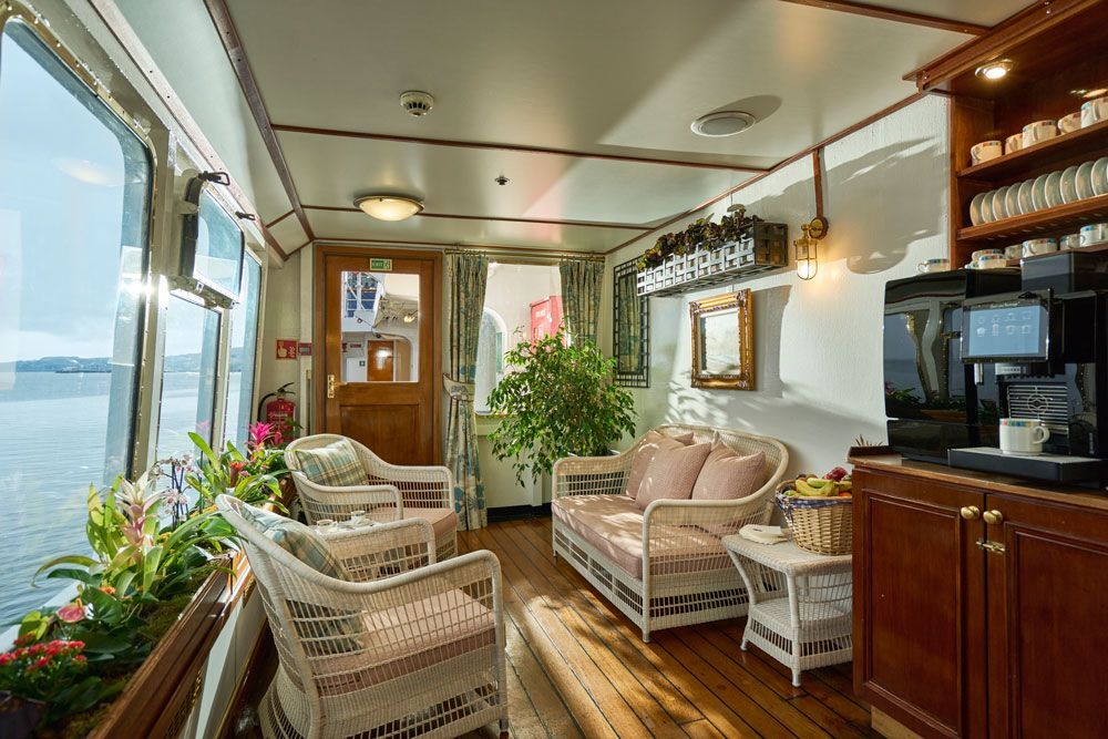 A living room on a boat with a couch , chairs , and a coffee maker.