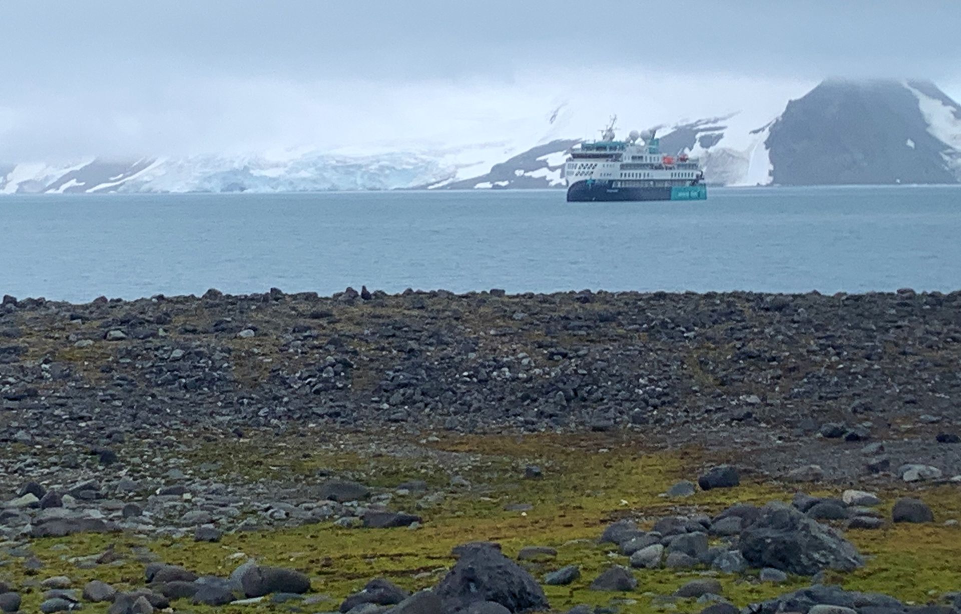 A boat is floating in the water near a rocky shoreline n Antarctica