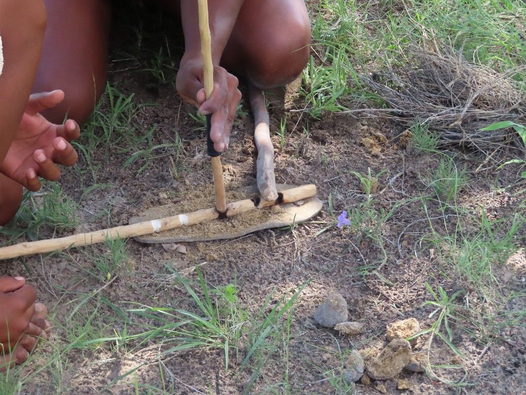 A person is using a stick to make a fire in the dirt.