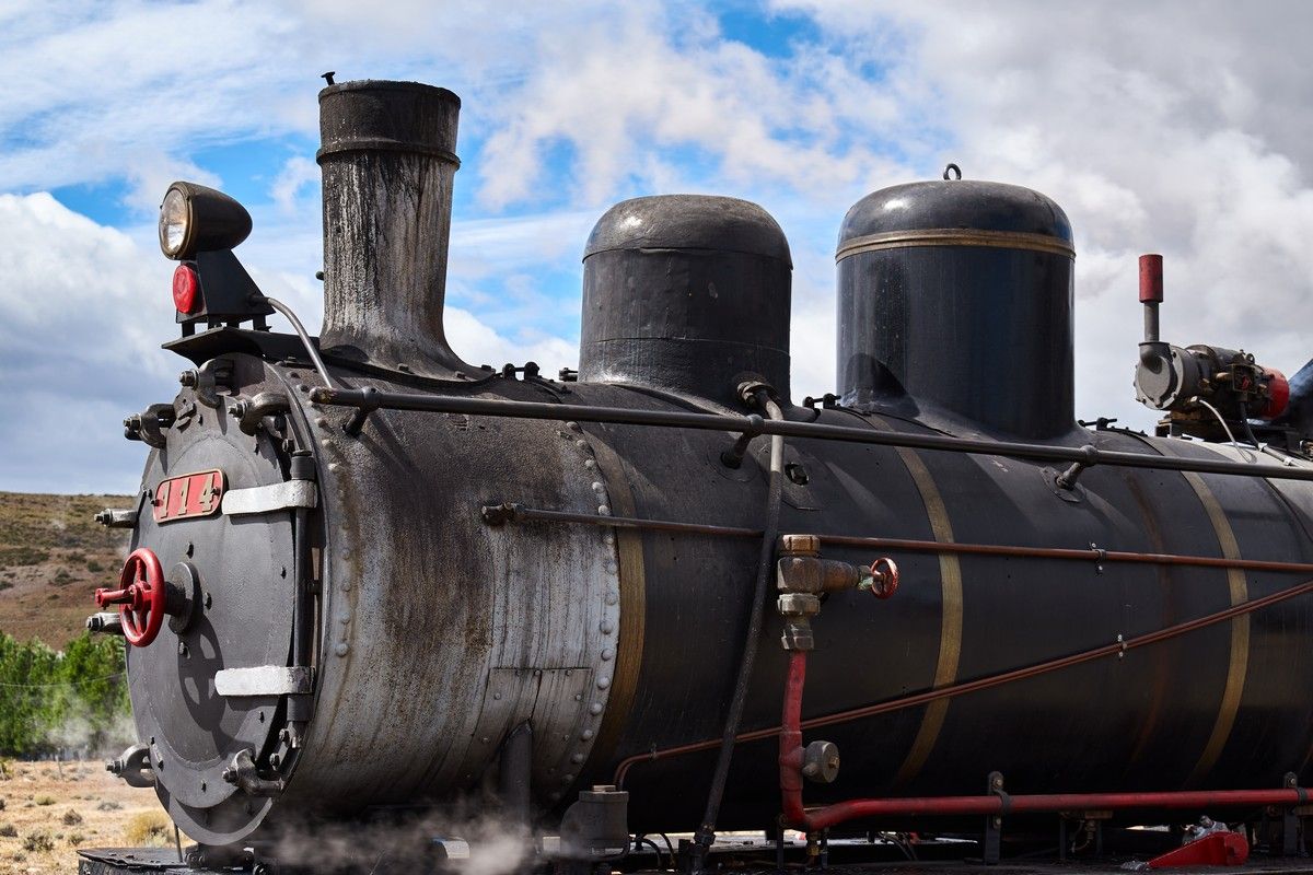 Black steam locomotive against a cloudy sky, smoke billowing.