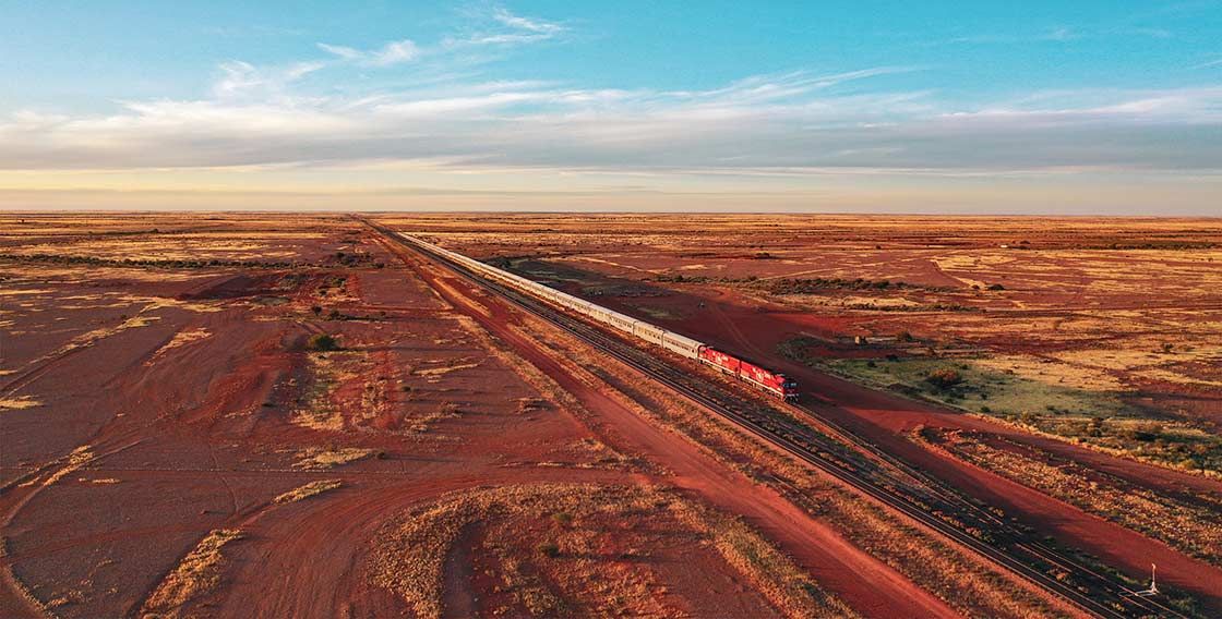 Train traveling across a red desert under a blue sky.