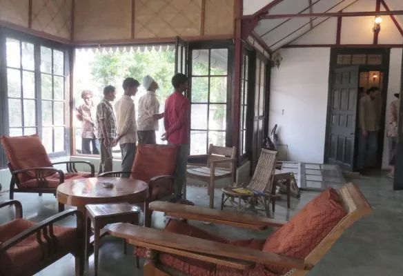 A group of people are standing in a living room with chairs and a table at Kaliabor Tea Estate