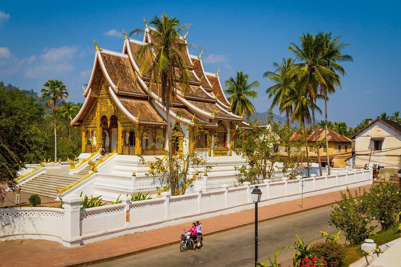 A couple is riding a motorcycle down a street in front of a temple in Luang Prabang in Laos