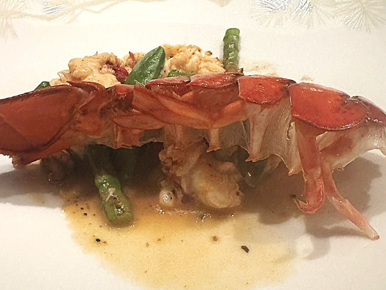 Lobster tail dish on a white plate with green beans and sauce.