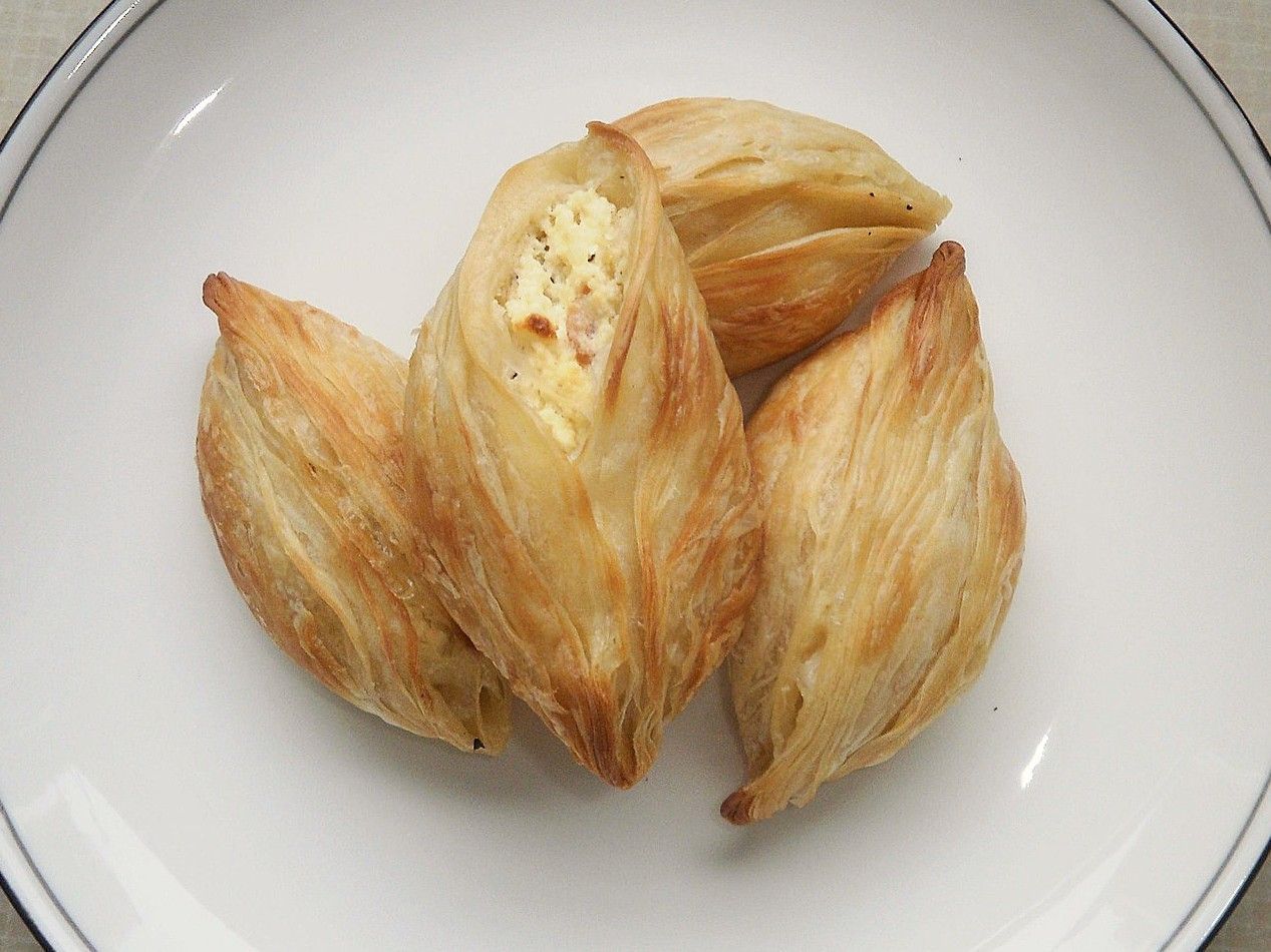 A white plate topped with three pastizzi with a blue rim.