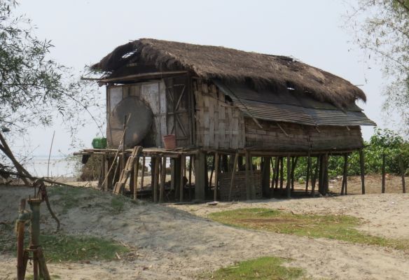 A small hut with a thatched roof is sitting on top of a field in the banks of the Brahmaputra river.