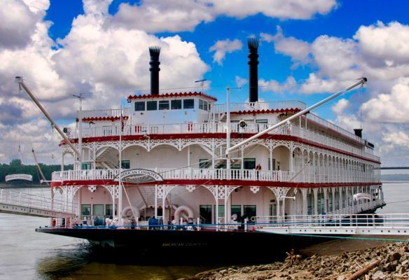 a large white and red steamboat is docked on the shore of a river Classic Mississippi River Cruise Boat