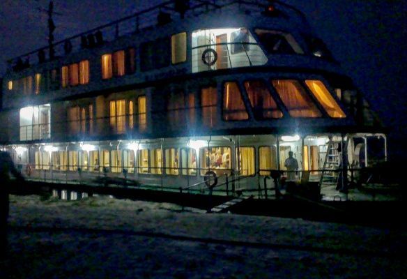 A large boat is lit up at night and sitting in on the banks of the Brahmaputra River in India